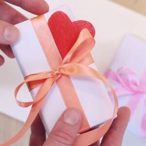 prikaz osobe koja u ruci drži mali poklon na kom je srce, u pozadini još jedan mali poklon