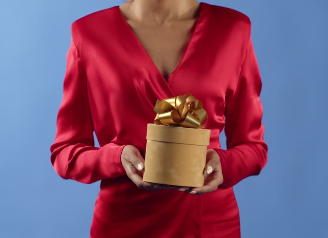 devojka u roze košulji drži zlatnu poklon kutiju sa zlatnom mašnom u rukama