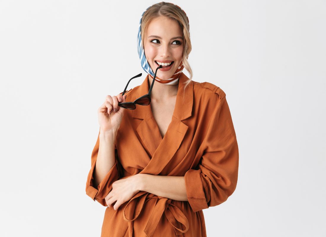 prikaz devojke sa svilenom maramom vezanom oko glave i crnim naočarama za sunce koje gricka suptilo zubima i smeši se